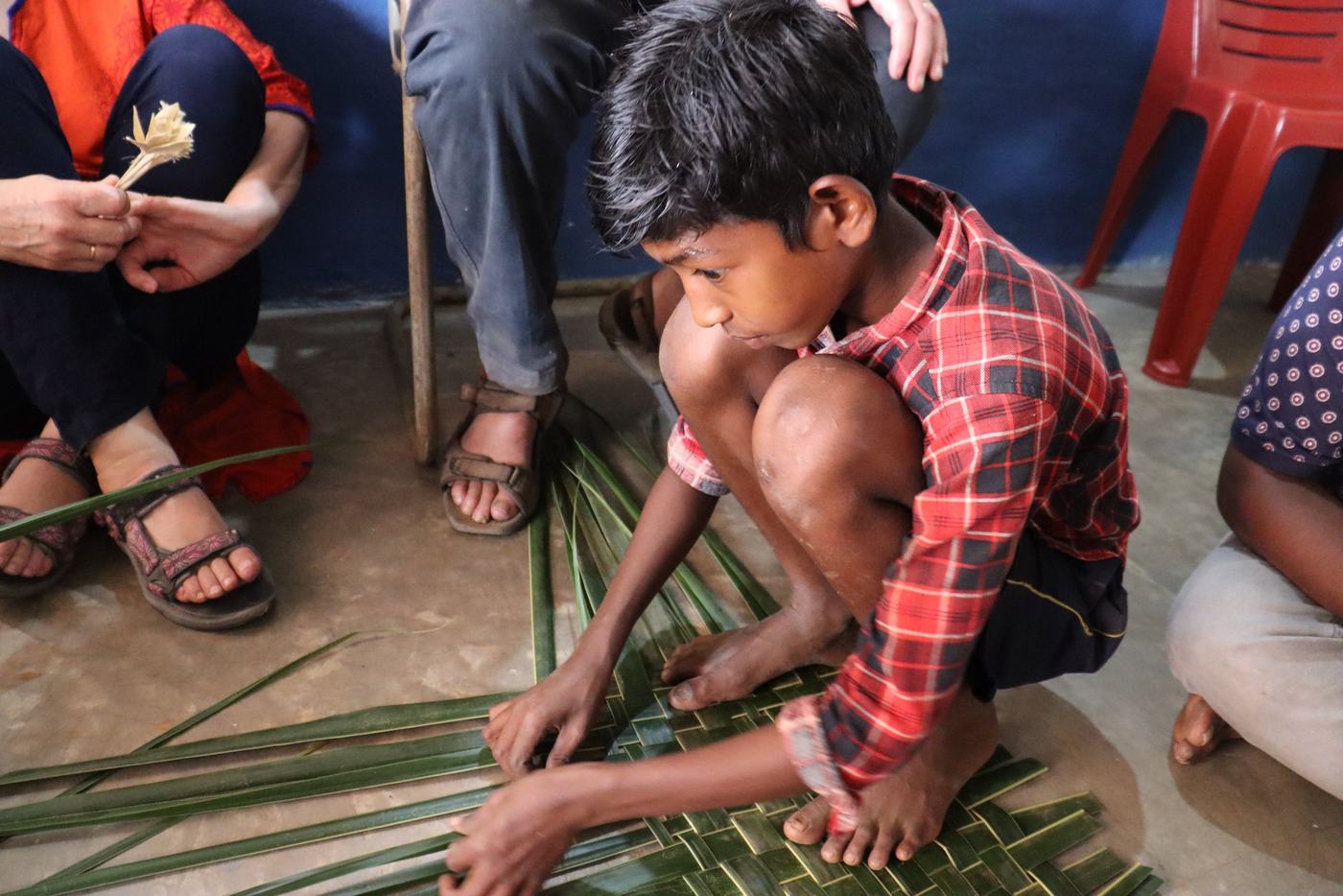 Weaving palm leaves with a member of staff